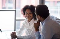 African american colleagues businessman and businesswoman talking having pleasant conversation discussion sitting in office, smiling mixed race woman enjoy chatting with male coworker at work break