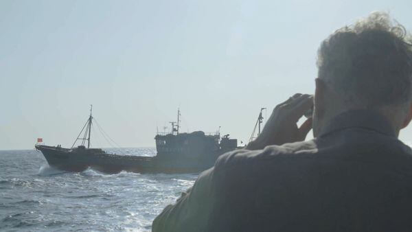 Ian Urbina looking at a Chinese vessel through binoculars.