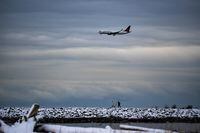 People bundled up for the cold weather walk on the Iona Jetty at Iona Beach Regional Park as an Air Canada plane prepares to land at Vancouver International Airport, in Richmond, B.C., on Sunday, December 26, 2021. THE CANADIAN PRESS/Darryl Dyck