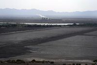FILE - A dried up portion of the Salton Sea stretches out with a geothermal power plant in the distance in Niland, Calif., Thursday, July 15, 2021. Demand for electric vehicles has shifted investments into high gear to extract lithium from geothermal wastewater around the rapidly shrinking body of water. The ultralight metal is critical to rechargeable batteries. (AP Photo/Marcio Jose Sanchez, File)