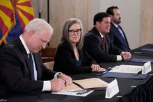 Arizona Supreme Court Chief Justice Robert Brutinel, left, signs the official Arizona general election canvass document as Arizona Democrat governor-elect and current Arizona Secretary or State Katie Hobbs, second from left, looks on while Arizona Republican Gov. Doug Ducey, second from right, and Arizona Attorney General Mark Brnovich, right, sit at the table as well during a signing ceremony at the Arizona Capitol in Phoenix, Monday, Dec. 5, 2022. (AP Photo/Ross D. Franklin, Pool)