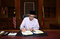 Malaysia's newly appointed Prime Minister Anwar Ibrahim signing a document as he clocks in to the Prime Minister office on his first day holding the premier position at Putrajaya, Malaysia November 25, 2022. Malaysian Department of Information/Wazari Wazir/Handout via REUTERS