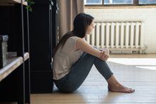 Side view of thoughtful depressed young woman sitting on floor at living room hugging knees and looking aside planning future life after dismissal, hard breakup, loss, getting health or work problems