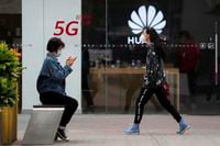 A woman wearing a face mask to help curb the spread of the coronavirus browses her smartphone as a masked woman walks by the Huawei retail shop promoting it 5G network in Beijing on Oct. 11, 2020. Chinese leaders are meeting to formulate an economic blueprint for the next five years that is expected to emphasize development of semiconductors and other technology amid a feud with Washington that is cutting off access to U.S. components for China's fledgling tech industries. (AP Photo/Andy Wong)