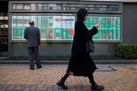 FILE PHOTO: A woman walks past a man examining an electronic board showing Japan's Nikkei average and stock quotations outside a brokerage, in Tokyo, Japan, March 20, 2023. REUTERS/Androniki Christodoulou/File Photo