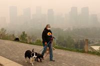 Wearing a protective mask, dog walker Leslie Kramer ventures out as heavy smoke from northern Alberta forest fires comes south to blanket the downtown area in Calgary, Tuesday, May 16, 2023. As air quality due to wildfire smoke remains poor in parts of Western Canada, health experts are advising people to stay inside as much as possible. THE CANADIAN PRESS/Larry MacDougal