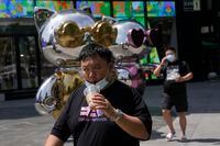 A man lowers his mask to drink from a cup as he past near a mall, July 13, in Beijing. China's economic growth plunged to 0.4 per cent over a year earlier in the latest quarter after Shanghai and other cities were shut down to fight coronavirus outbreaks, but the government said a "stable recovery" is underway.