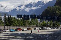 People pass by a row of cars waiting to board the ferry to Vancouver Island, as travel restrictions in the province lift, June 15, 2021. (Cole Burston/The Globe and Mail)