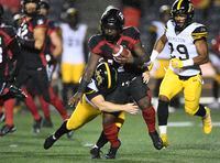 Hamilton Tiger-Cats kicker Michael Domagala (19) wraps his arms around Ottawa Redblacks wide receiver DeVonte Dedmon (17) during first half CFL football action in Ottawa on Wednesday, Sept. 22, 2021. THE CANADIAN PRESS/Justin Tang