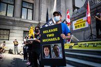 A man holds a sign with photographs of Michael Kovrig and Michael Spavor, who have been detained in China since December, 2018, as people gather for a rally in support of Hong Kong democracy, in Vancouver, B.C., Sunday, Aug. 16, 2020. THE CANADIAN PRESS/Darryl Dyck