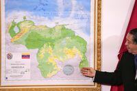 FILE - Chairman of the Special Commission for the Defense of Guyana Essequibo Hermann Escarra, stands next to Venezuela's new map that includes the Essequibo territory, a swath of land that is administered and controlled by Guyana but claimed by Venezuela, during an unveiling ceremony in Caracas, Venezuela, Dec. 8, 2023. Venezuelan military officials said Saturday, Dec. 30, 2023, that they will continue to deploy nearly 6,000 troops until a British military vessel sent to neighboring Guyana leaves the waters off the coast of the two South American nations. (AP Photo/Matias Delacroix, File)