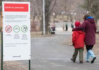 People walk by a COVID-19 information sign in a city park in Montreal, Sunday, April 5, 2020, as Coronavirus COVID-19 cases rise in Canada and around the world. THE CANADIAN PRESS/Graham Hughes