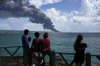 People watch a huge rising plume of smoke caused by a blaze at the Matanzas Supertanker Base, in Matazanas, Cuba, Saturday, Aug. 6, 2022. Cuban authorities say lightning struck a crude oil storage tank at the base, causing a fire that led to four explosions which injured more than 50 people. (AP Photo/Ramon Espinosa)
