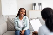 Successful therapy. Young female client having consultation with psychologist, grateful for professional help at clinic. Happy black lady speaking with her psychotherapist, solving emotional problem
