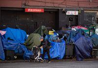 A man using a rolling walker passes tents set up on the sidewalk at a sprawling homeless encampment on East Hastings Street in the Downtown Eastside of Vancouver on Aug. 16, 2022. THE CANADIAN PRESS/Darryl Dyck