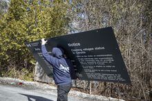 A worker wearing a sweatshirt from a sign company removes a sign with information about claiming asylum at the unofficial border crossing point at Roxham Road, in Québec. 
