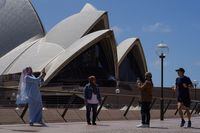 A jogger runs past people taking pictures in front of the Sydney Opera House in the wake of coronavirus disease (COVID-19) regulations easing, following months of lockdown orders to curb an outbreak, in Sydney, Australia, October 19, 2021. REUTERS/Loren Elliott