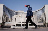 FILE PHOTO: A man wearing a mask walks past the headquarters of the People's Bank of China, the central bank, in Beijing, China, as the country is hit by an outbreak of the new coronavirus, February 3, 2020. REUTERS/Jason Lee/File Photo
