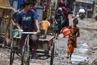 A Rohingya refugee girl gestures as she walks through a muddy street at a refugee camp on the World Refugee Day, in New Delhi on June 20.