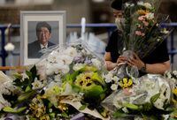 A mourner offers flowers next to a picture of late former Japanese Prime Minister Shinzo Abe, who was shot while campaigning for a parliamentary election, on the day to mark a week after his assassination at the Liberal Democratic Party headquarters, in Tokyo, Japan July 15, 2022.  REUTERS/Issei Kato