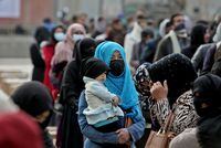FILE PHOTO: An Afghan woman holds her child as she and others wait to receive package being distributed by a Turkish humanitarian aid group at a distribution centre in Kabul, Afghanistan, December 15, 2021. REUTERS/Ali Khara