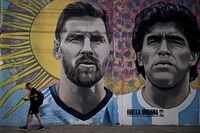 A man passes by a mural depicting Argentine football stars Lionel Messi (L) and late Diego Maradona (R) in the eve of Qatar 2022 World Cup final football match between Argentina and France in Buenos Aires, on December 16, 2022. (Photo by Luis ROBAYO / AFP) (Photo by LUIS ROBAYO/AFP via Getty Images)