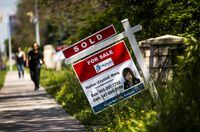 A pedestrian walks towards a 'for sale' sign in front of a home in Toronto.