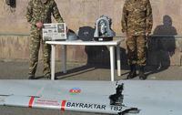 Two soldiers at an Armenian military compound pose with a wing of a downed Turkish-made Bayraktar TB2 drone and the Canadian-made L3 Harris Wescam airstrike targeting gear. Armenia says all the parts were on a drone captured in the Nagorno-Karabakh conflict. One soldier is holding the October 29, 2020 front page of the Hayastani Hanrapetutiun newspaper. Date of photo is October 29, 2020. Photo credit: Neil Hauer.