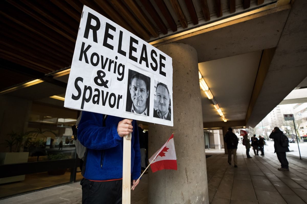 A young man holds a sign bearing photographs of Michael Kovrig and Michael Spavor.