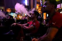 A Moroccan smoke a vape as he watch from a tv in Rabat, Morocco the World Cup semifinal soccer match between France and Morocco that is being played in Qatar, on Wednesday, Dec. 14, 2022. (AP Photo/Ben Curtis)