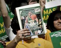 FILE - A George Mason University fan holds up a Sports Illustrated magazine at a send off for the team, March 29, 2006, in Fairfax, Va. Sports Illustrated is the latest media company damaged by being less than forthcoming about who or what is writing its stories. The website Futurism reported that the once-grand magazine used articles with “authors” who apparently don't exist, with photos generated by AI. The magazine denied claims that some articles themselves were AI-assisted, but has cut ties with a vendor it hired to produce the articles. (AP Photo/Lawrence Jackson, File)