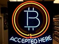 In this Feb. 7, 2018 file photo, a neon sign hanging in the window of Healthy Harvest Indoor Gardening in Hillsboro, Ore., shows that the business accepts bitcoin as payment.