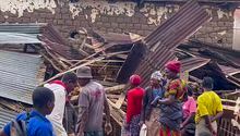 People stand next to a collapsed building in western Rwanda on Wednesday, May 3, 2023. Torrential rains caused flooding in western and northern Rwanda, killing more than 100 people, a public broadcaster said Wednesday. (RwandaTV via AP)