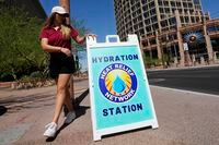 FILE - Julia Marturano, of The City of Phoenix Heat Response Program, places a sign out on the sidewalk directing those who need water and other items to a hydration station as temperatures are expected to hit 119-degrees Thursday, July 20, 2023, in Phoenix. Record setting temperatures are expected Saturday, Aug. 19, across Texas as the southwestern U.S. continues to bake during a scorching summer. (AP Photo/Ross D. Franklin, File)