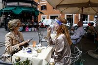A woman sips her coffee from under her facial protection at a cafe with outdoor tables in Rome Monday, May 18, 2020. Italy is slowly lifting restrictions after a two-month coronavirus lockdown. (Cecilia Fabiano /LaPresse via AP)