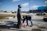 A woman places flowers at the foot of a statue depicting Walter Gretzky outside the Wayne Gretzky Sports Centre in Brantford, Ont. following the news of his passing, Friday, March 5, 2021. THE CANADIAN PRESS/Cole Burston