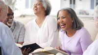 Active group of happy seniors laugh as they enjoy life in a senior living community. They are participating in a book club.