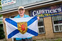 Angus Capstick, stands holding a Nova Scotia flag outside of his store Capstick's Novelties and More located in Sydney, NS on July 30, 2021
