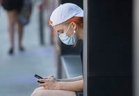 A woman wears a face mask as she browses on her phone in Montreal, Sunday, August 16, 2020, as the COVID-19 pandemic continues in Canada and around the world. THE CANADIAN PRESS/Graham Hughes