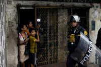 A family from Iquita takes shelter at the door of their house, while they watch the police guarding the demonstrators of the march against the congress and the new Peruvian government pass by in astonishment in Iquitos, Peru on Dec. 15, 2022. Patrick Murayari/TGAM
