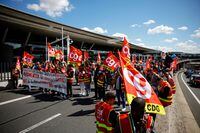 Paris-Charles de Gaulle airport employees on strike hold French CGT labour union flags as they walk outside the Terminal 2F during a protest against low wages as inflation hits France, at the Paris-Charles de Gaulle airport.