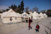 Children walk past tents in a makeshift camp in Antakya, southern Turkey, on February 22, 2023. - A 6.4-magnitude earthquake has rocked Turkey's southern province of Hatay and northern Syria, killing six people and sparking fresh panic after a massive February 6 tremor left nearly 45,000 dead in both countries. (Photo by Sameer Al-DOUMY / AFP) (Photo by SAMEER AL-DOUMY/AFP via Getty Images)