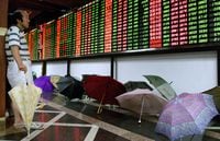 FILE PHOTO: A Chinese investor monitors share prices in front of dozens of umbrellas left to dry at a Shanghai securities firm August 9, 2001./File Photo