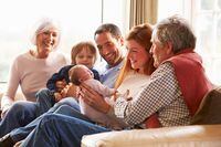 Multi Generation Family Sitting On Sofa With Newborn Baby Smiling