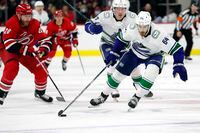 Vancouver Canucks' Tyler Motte (64) moves the puck after taking it from Carolina Hurricanes' Ian Cole (28) during the third period of an NHL hockey game in Raleigh, N.C., Saturday, Jan. 15, 2022. (AP Photo/Karl B DeBlaker)