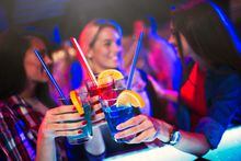 Blurred image of three cheerful female friends  having fun in the night club, drinking cocktails, cheering, smiling, bonding, clubbing. Focus is on cocktali  drinks in the foreground.