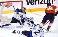 Apr 15, 2022; Sunrise, Florida, USA;  Florida Panthers center Maxim Mamin (98) slides the puck under Winnipeg Jets goaltender Eric Comrie (1) for a goal during the third period at FLA Live Arena. Mandatory Credit: Jim Rassol-USA TODAY Sports