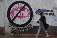 A woman with a dog walks by a mural signed by Partizan club fans, reads: "Turn on your brain, switch off Pink," referring to Pink TV's overwhelming pro-government propaganda and violent content on reality shows, in Belgrade, Serbia, Friday, May 12, 2023. A drawing demanding a ban on the Pink television in Serbia has appeared on the wall where mural of convicted war criminal, former Bosnian Serb military chief Ratko Mladic was previously painted. Calls to ban Pink and another TV with similar content have grown since 17 died in two mass shootings last week. (AP Photo/Darko Vojinovic)