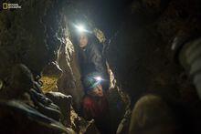In this photo provided by National Geographic, National Geographic Explorer-in-Residence Lee Berger's daughter, Megan, and underground exploration team member Rick Hunter navigate the narrow chutes leading to the Dinaledi Chamber of the Rising Star Cave in South Africa in 2014, where fossil elements belonging to Homo naledi, a new species of human relative, were discovered. In research released on Monday, June 5, 2023, scientists say they've found evidence that the ancient human cousin buried its dead and carved symbols into cave walls, actions previously tied only to bigger-brained species. (Robert Clark/National Geographic via AP)