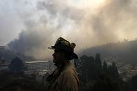 A firefighter is silhouetted against a smoke-filled sky as a forest fire spreads into Vina del Mar, Chile, Saturday, Feb. 3, 2024. Officials say intense forest fires burning around a densely populated area of central Chile have left several people dead and destroyed hundreds of homes. (AP Photo/Esteban Felix)